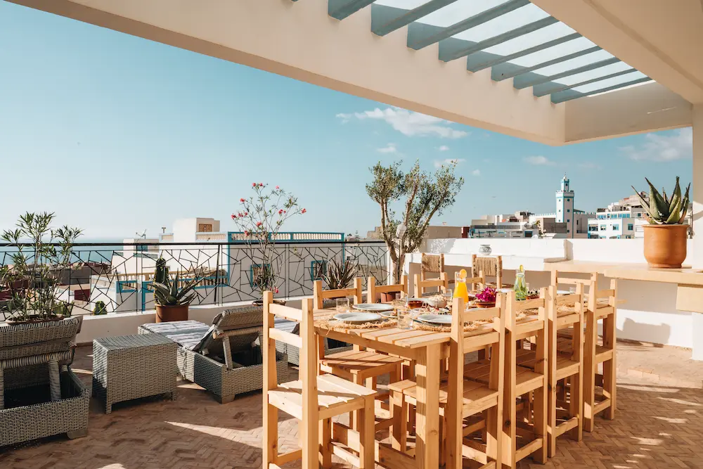 A wooden dining table and lounge seating on the roof terrace, with the town behind