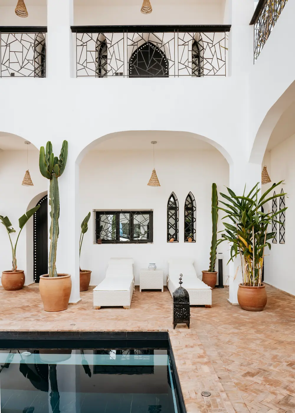 The villa courtyard, with a pool, white loungers, arched balconies and potted plants
